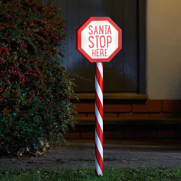Novelty 'Santa Stop Here' sign with candy cane design on a grassy area.