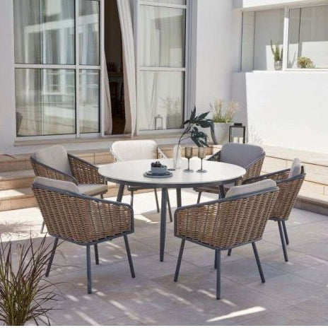 Outdoor patio set with round table and chairs on a patio with plants and building in the background