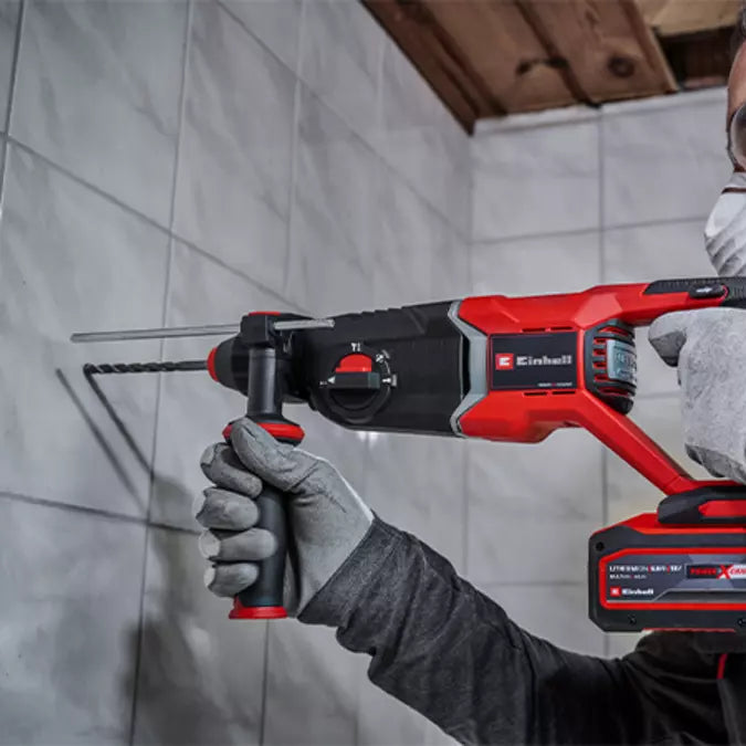 Person using a red and black rotary hammer drill in a tiled room.