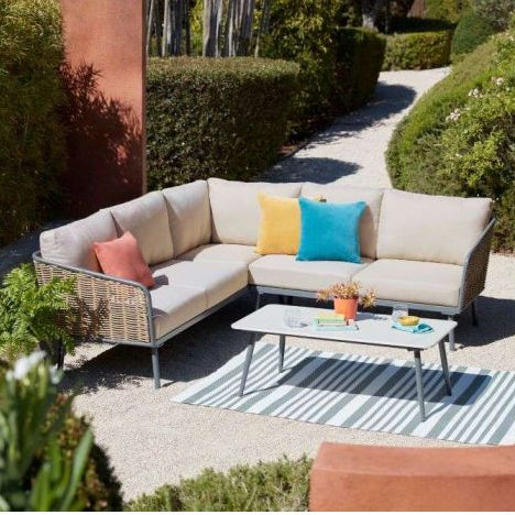 Outdoor patio set with a sectional sofa and coffee table in a garden setting.