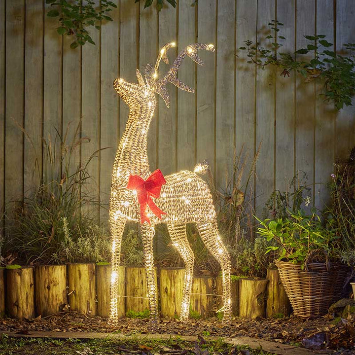 Decorative lighted deer with a red bow in a garden setting